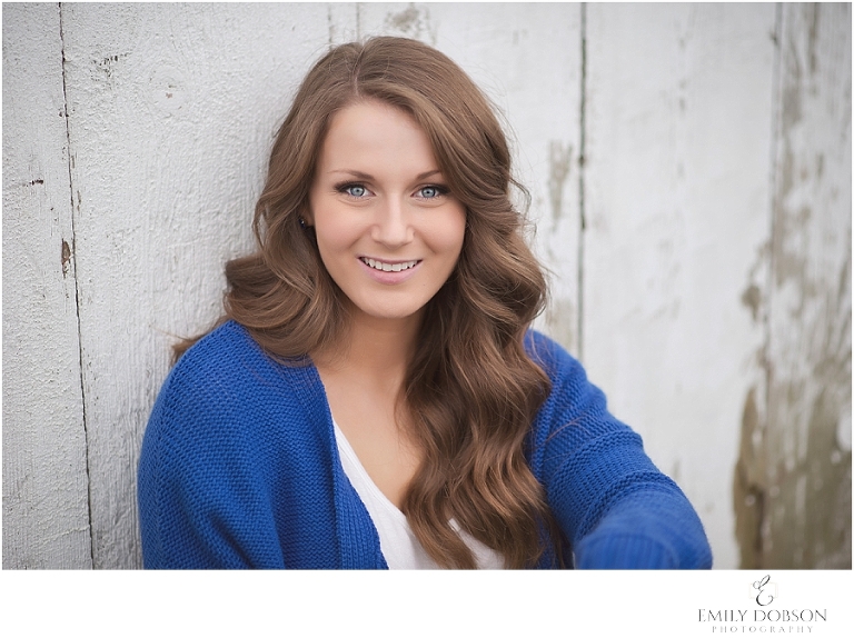 HS senior posing in front of a wooden shed on her farm