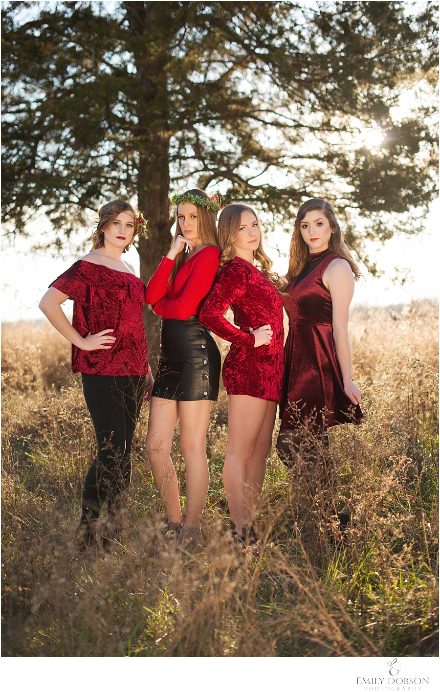 Four high school seniors wearing Christmas red and burgandy in a field with golden haze coming from behind