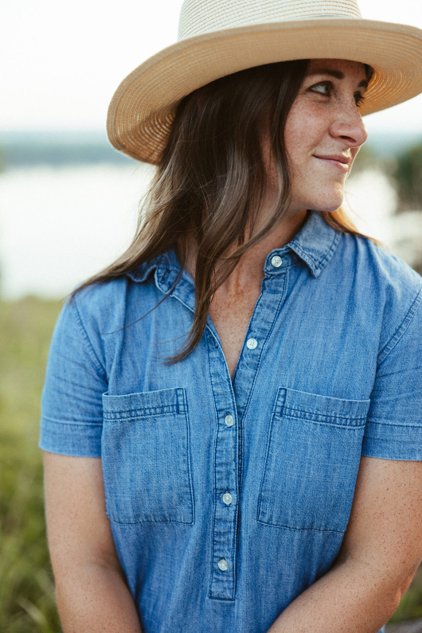 36-year-old woman wearing a denim dress and a hat looking over her shoulder